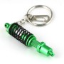 Metallinen “iskunvaimennin” -avaimenperä vihreä-mustana, avainrengas ja jousitettu rakenne selkeästi esillä valkoisella taustall