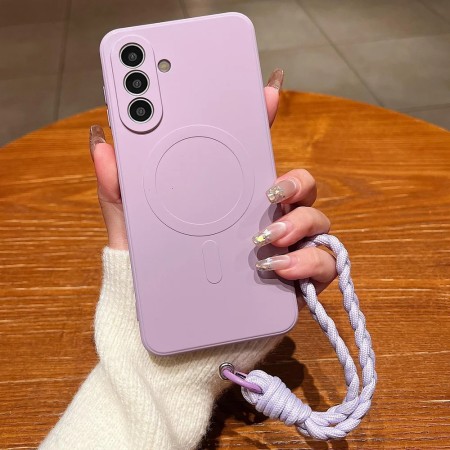 Samsung Galaxy A57 5G lilanvärinen MagSafe silikonisuojakuori rannenauhalla kädessä puupöydällä.